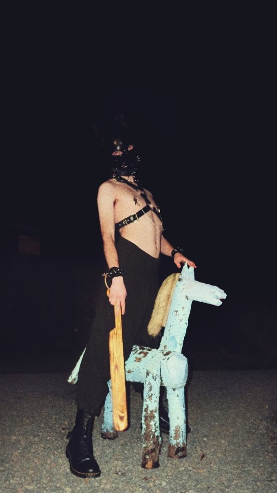 Mollishund stands in towering darkness, astride a pale wooden horse; wielding a long wooden paddle 👏🍑