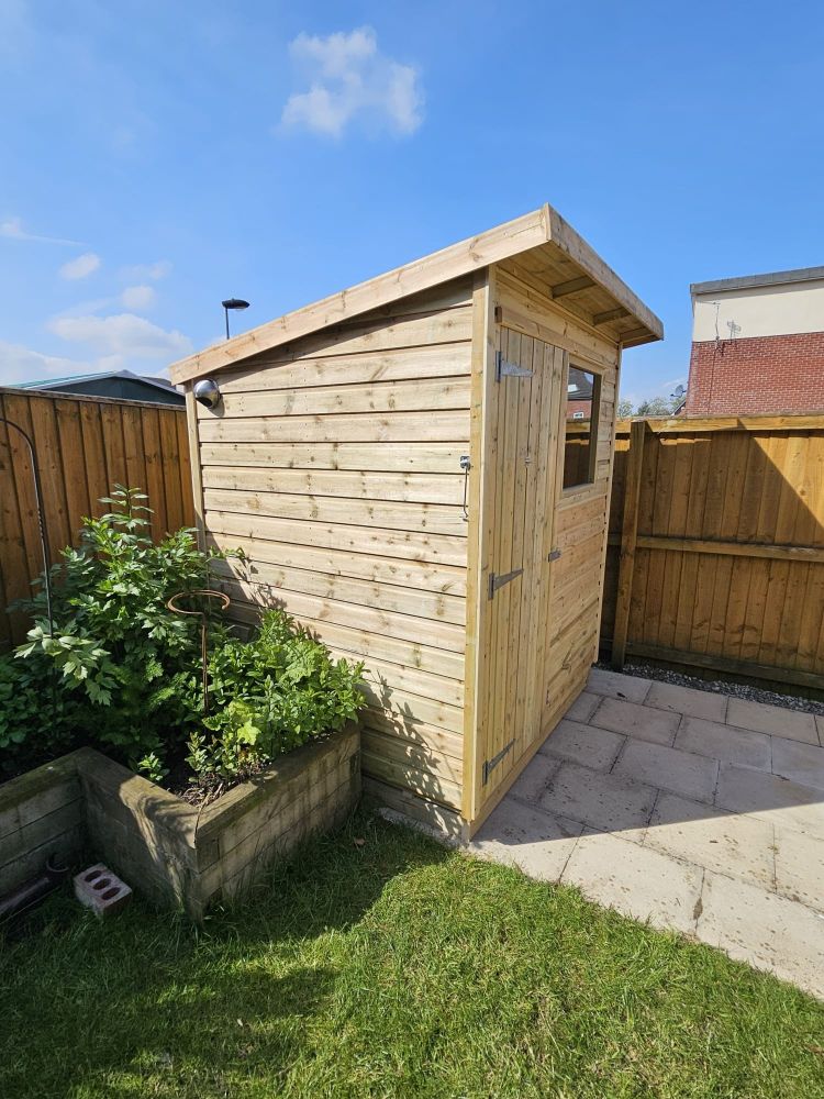 New pent shed on a patio behind a herb planter