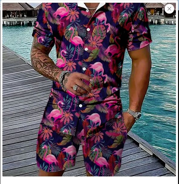 Tanned and tattoed man wearing a shirt and shorts ensemble in dark midnight blue with pink flamingoes and purple/blue plants.  The colours are striking against the tanned skin.