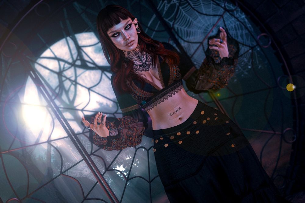 Secondlife avatar making witchy pose in front of a spooky gate, moon, and spider web.