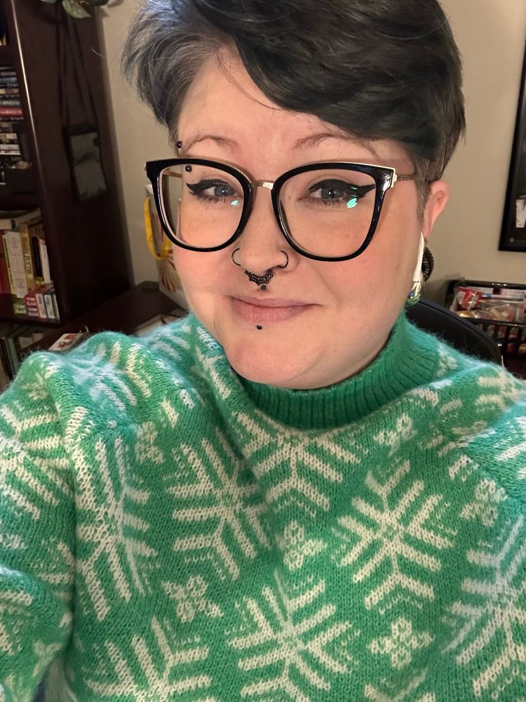 Selfie of me with short black hair and a green snow sweater 