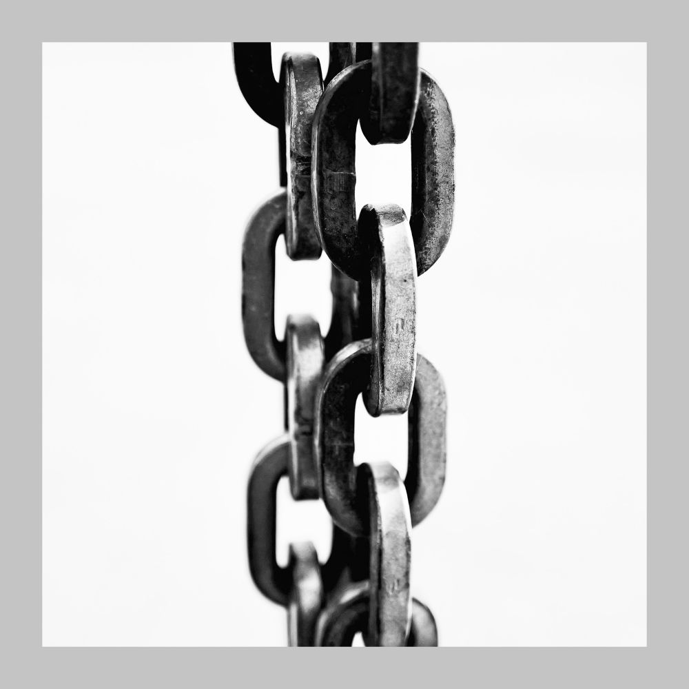 High contrast monochrome closeup of dark chains hanging against a white background