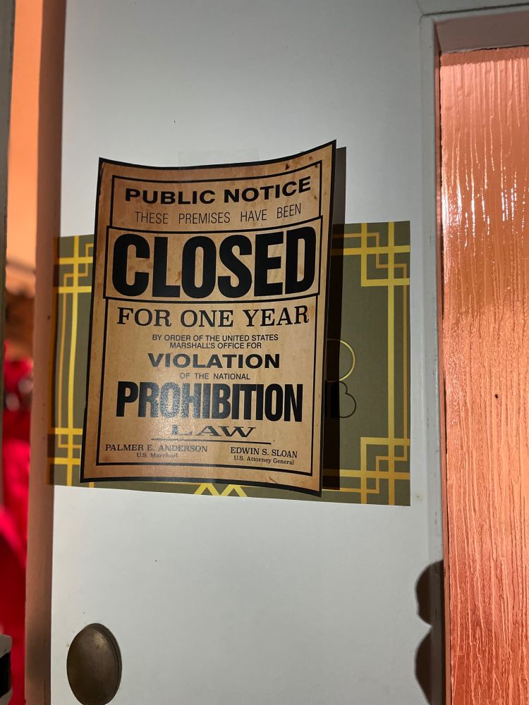 A front door of a house with an old-timey looking poster on it. The text reads "Public notice: these premises have been closed for one year by order of the United States Marshalls Office for violation of the national Prohibition law."