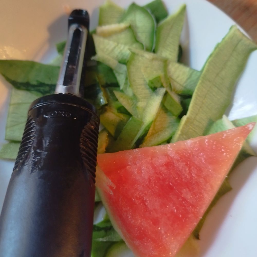 Bowl with vegetable peeler, green perks and pink triangle of food.