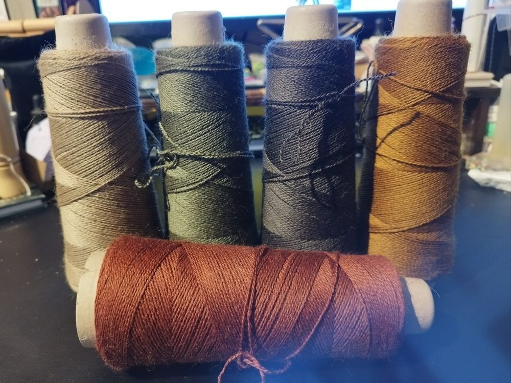 5 cones of yarn for using as a warp in weaving, all in muted colors.