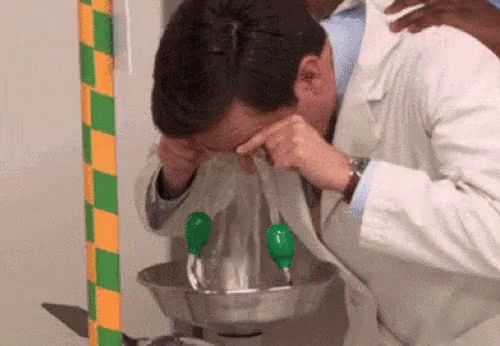 a man in a lab coat is washing his eyes in a bowl of water