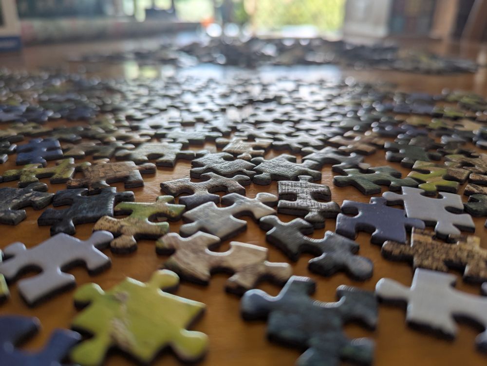 A photo of part of a table top covered with partially sorted jigsaw puzzle pieces