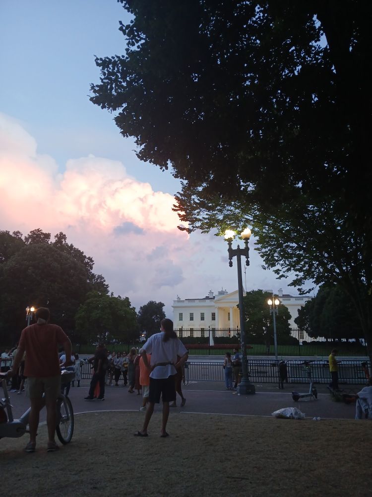 The White House with people in front and thunderclouds in the background.