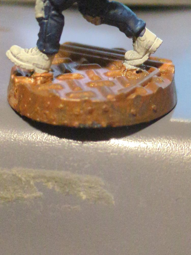 Close up of a figurine base. The paint is bronze, but has beaded up to create a 'pimpling' effect.