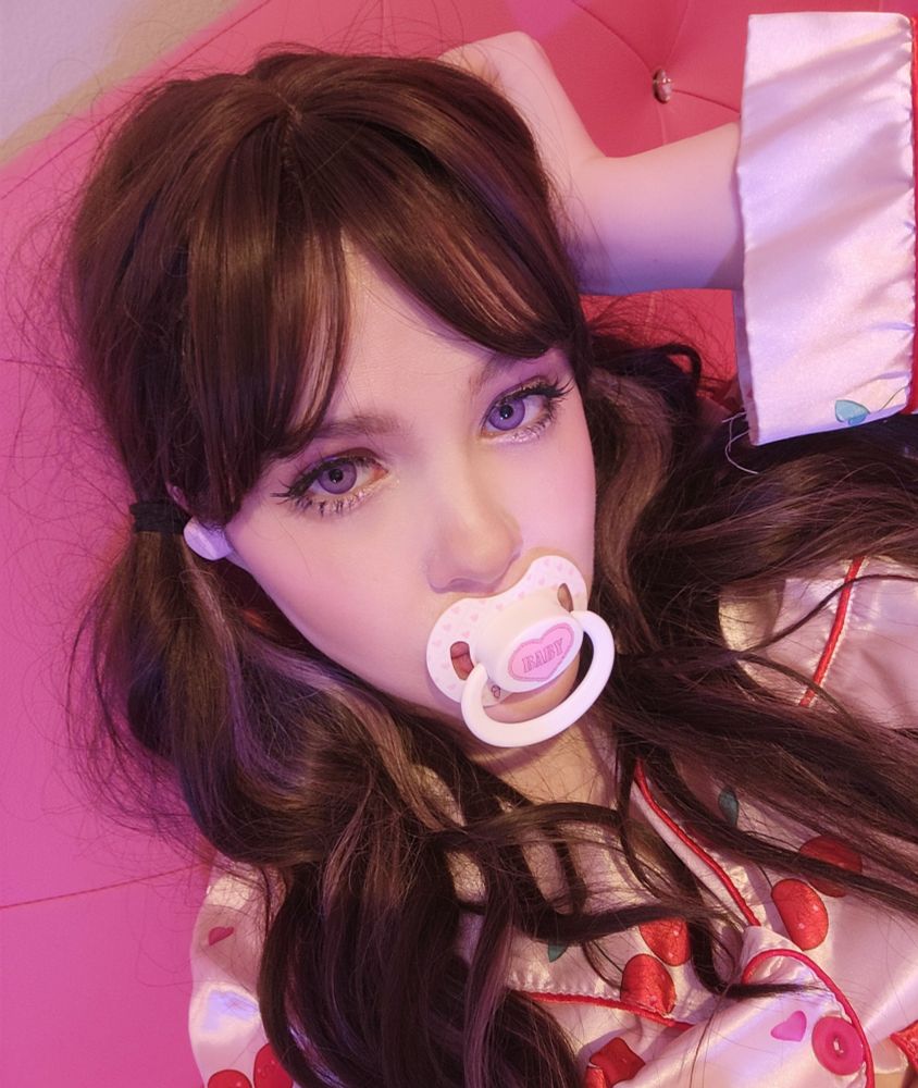 Aeris with a white BABY pacifier in her mouth. She's wearing satin cherry print pjs and has pigtails.