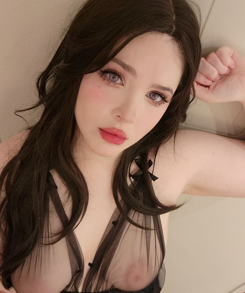 Aeris has dark brunette, wavy hair. Her purple eyes are striking against dark brown eyeshadow and vivid red lips. Her breasts are visible through sheer black fabric. One arm is in the air as if being held up by you against the wall.