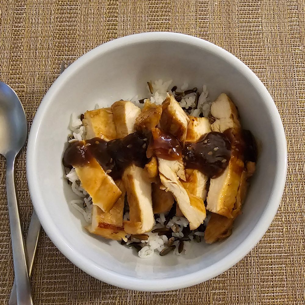 Picture of a white ceramic bowl with grilled teriyaki chicken that was marinated overnight with homemade teriyaki sauce, on a bed of basmati and wild rice with a little more sauce topping it off.