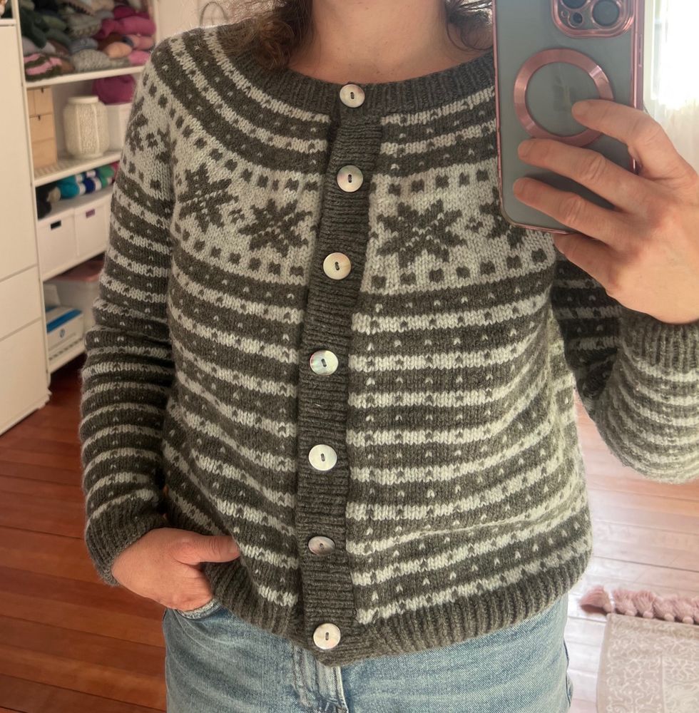 Ein Spiegelselfie von mir. Die Sonne scheint in das Zimmer. Ich trage eine selbst gestrickte Jacke mit einem Sternenmotiv in grau auf hellblauem Grund. 