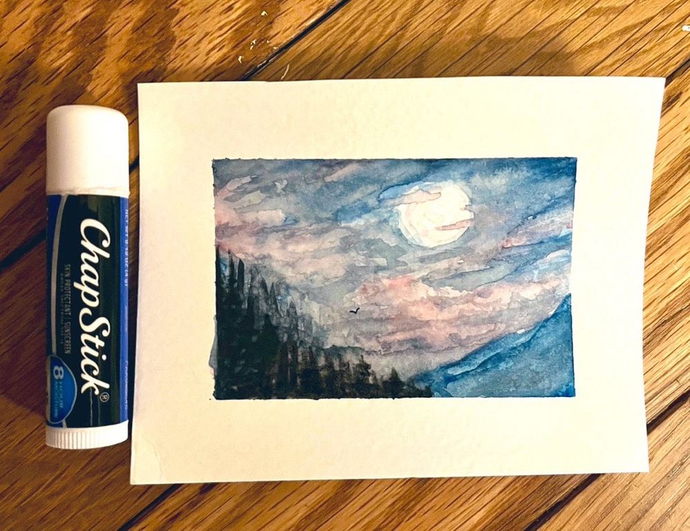 Tiny watercolor of a mountain range next to a chap stick for scale 