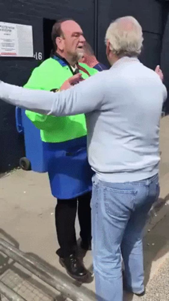 a man wearing a green vest is carrying a blue trash can