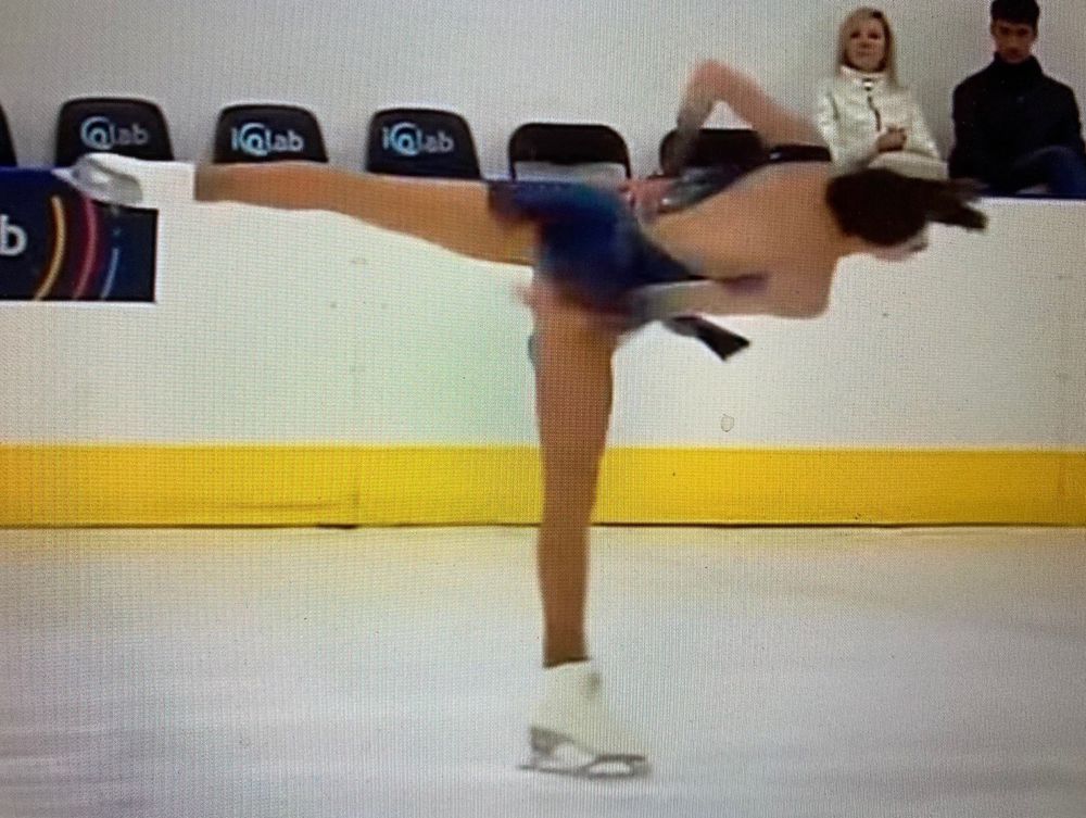 Figure skater in a camel spin, making a shark fin shape with her upper arm. 