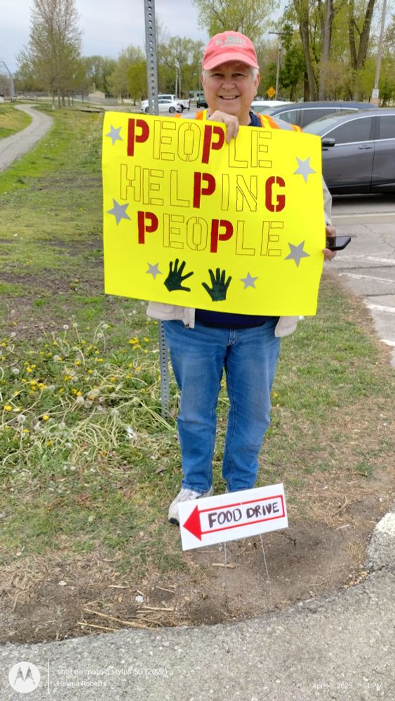 A volunteer holding a sign that reads "People Helping People" 