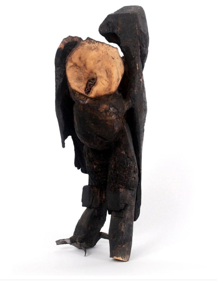 A bird sculpture stands alone in a white field. The sculpture is of an owl, it's made is wood with metal claws on one foot. The natural knots in the wood create the face- especially the beak of the bird. It has thick, chunky legs and the bark that originally covered the piece is wood have been carved into the wings. This piece was created while i was pregnant with the sculptors child- our daughter- during which time I'd had prophetic dreams about owls. When our daughter was born she had a cleft lip, a fuzzy head and big sparkly eyes: she looked like an OWL! So her middle name is the the Welch word for owl, which is Tylluan. We knew who age was before she was born!