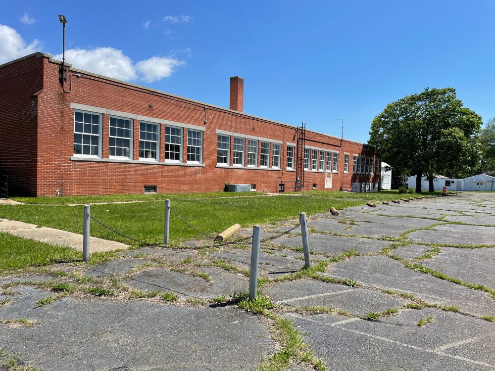 The side of a low brick building, with windows all along the side, in an asphalt parking lot.