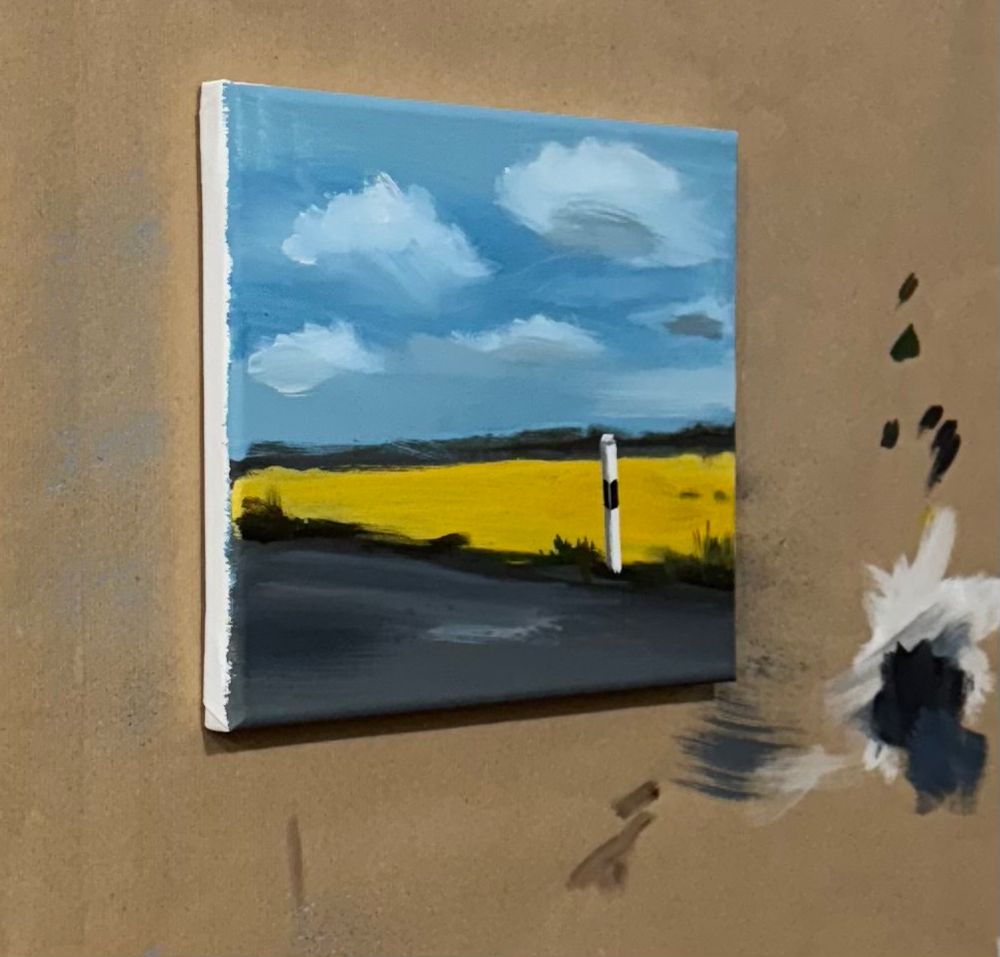 Acrylic painting showing a yellow rapeseed field under a blue sky at the roadside. 
