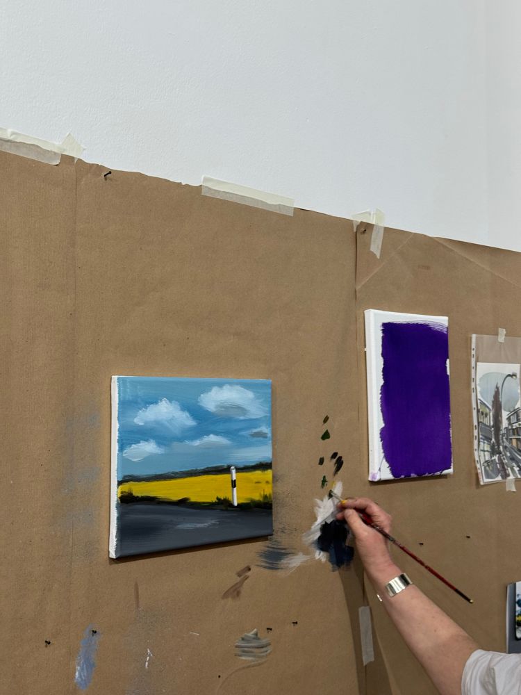 Several partially painted canvases on the wall. You can also see my hand with a brush mixing paint. 