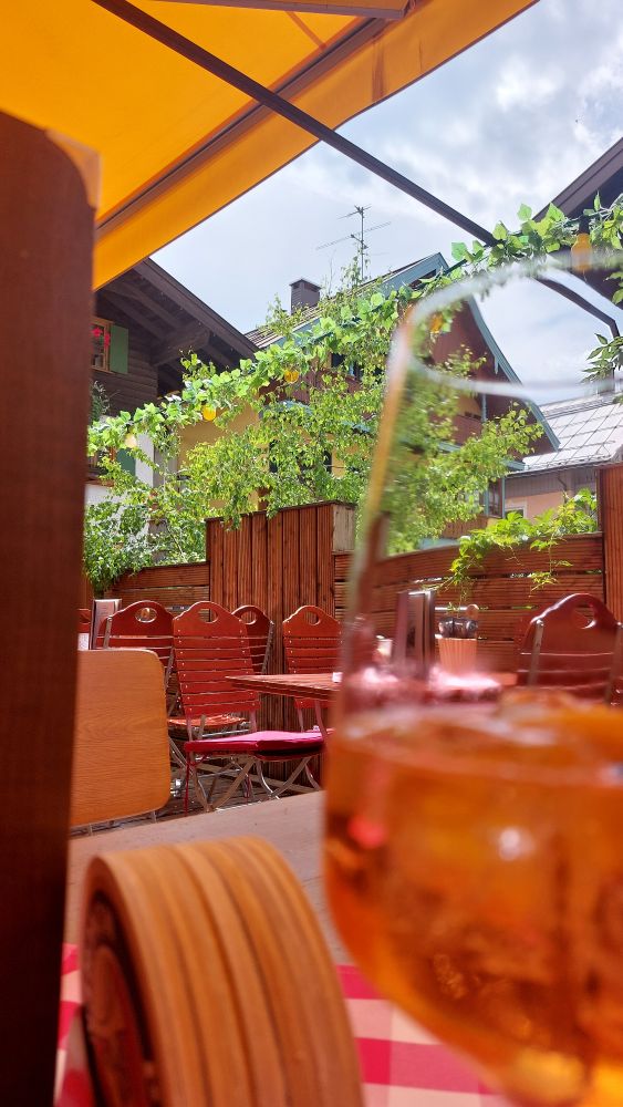 Im Vordergrund ein Glas Aperol, aufgenommen in einem Biergarten 