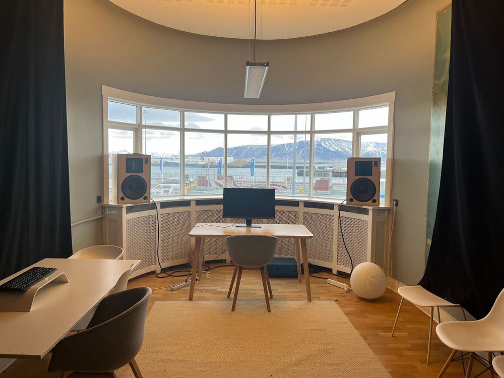 A modern office desk looking out of a bay window over a view of mountains and harbour
