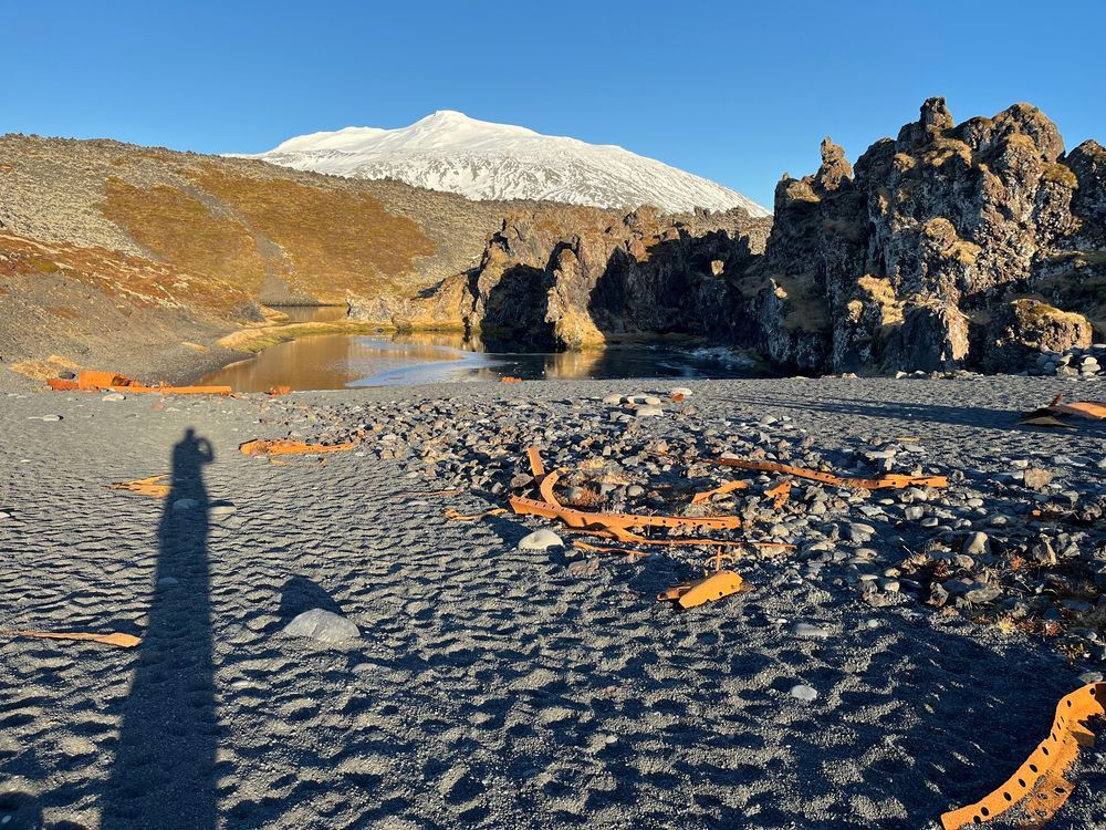 Rusty scrap remains of the Grimsby trawler wrecked on a black sand beach with a glacier behind it