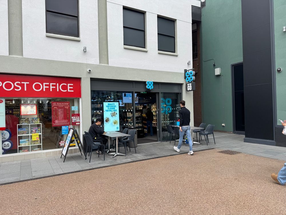 A co op food to go shop with chairs and tables outside and a post office next door