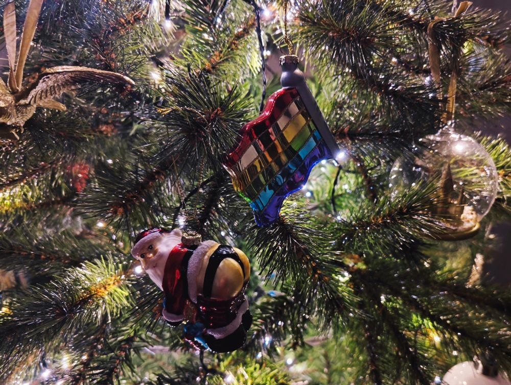 Pride-flag und "Sexy-Santa" Weihnachtsbamkugel an Tannenzweigen hängend.