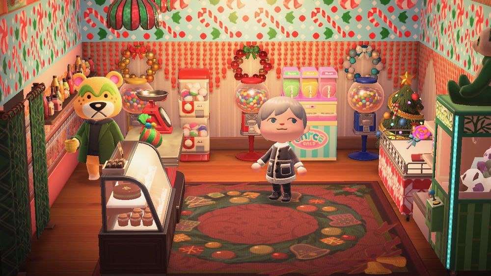 An ACNH screenshot of Nate's home interior decorated like a candy shop with candy-covered wallpaper and a holiday wreath rug.  To the right is a stuffed animal claw machine, a candy display, and a Christmas tree.  Straight ahead is a smoothie machine, candy machines, and a gachapon machine. To the left, Nate is standing behind the counter looking at the camera.  On the counter is a gift-wrapped item scale and next to the counter is a a glass pastry case. Nate is a large yellow-furred bear with green eyebrows wearing a matching green coat over a black shirt.