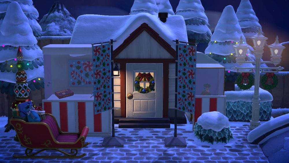 An ACNH screenshot of a snow-covered villager's home exterior decorated like a candy shop with candy-covered banners and signs, candy in display windows, and a bright red sleigh parked in front.