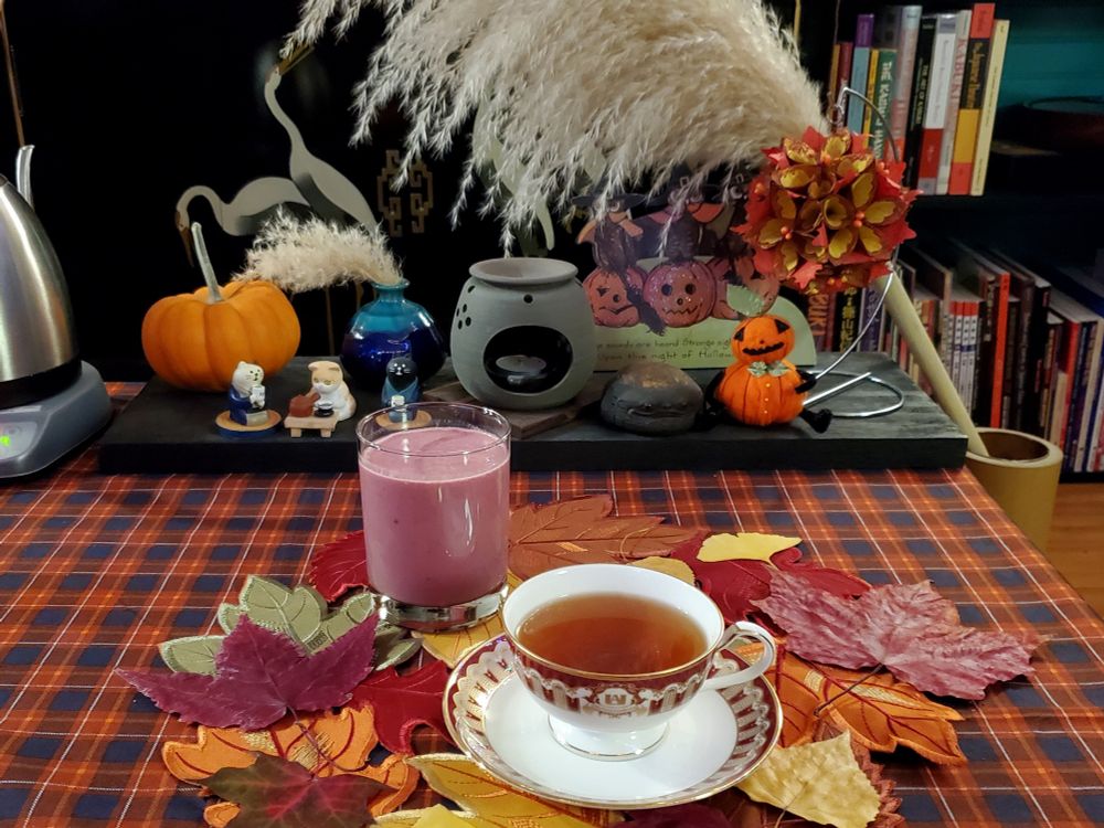 A table decorated for autumn and set with a tea cup filled with tea and a glass filled with a blackberry smoothie.