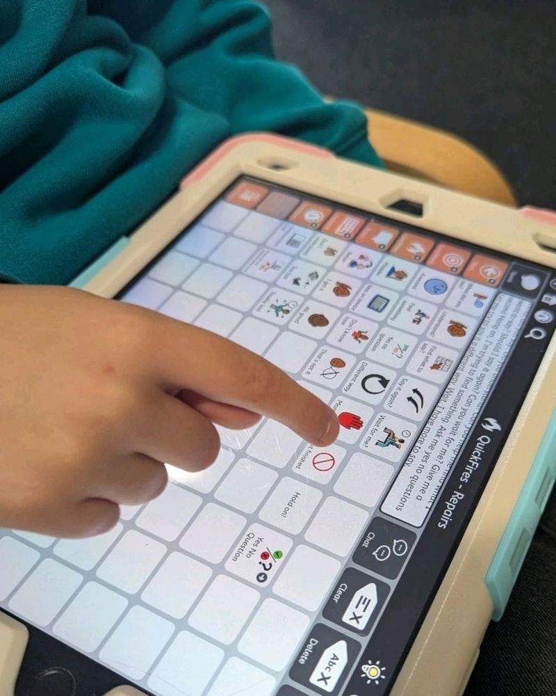 Photo shows a child holding an iPad with the TD Snap communication app displayed on screen. The page has vocabulary related to communication repairs. The child is pointing to a symbol and the message window is full of vocabulary and shows various buttons have been pressed.
