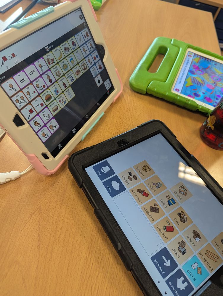 Photo of a desk with three iPads, two showing difference communication apps and one showing a children's video. 