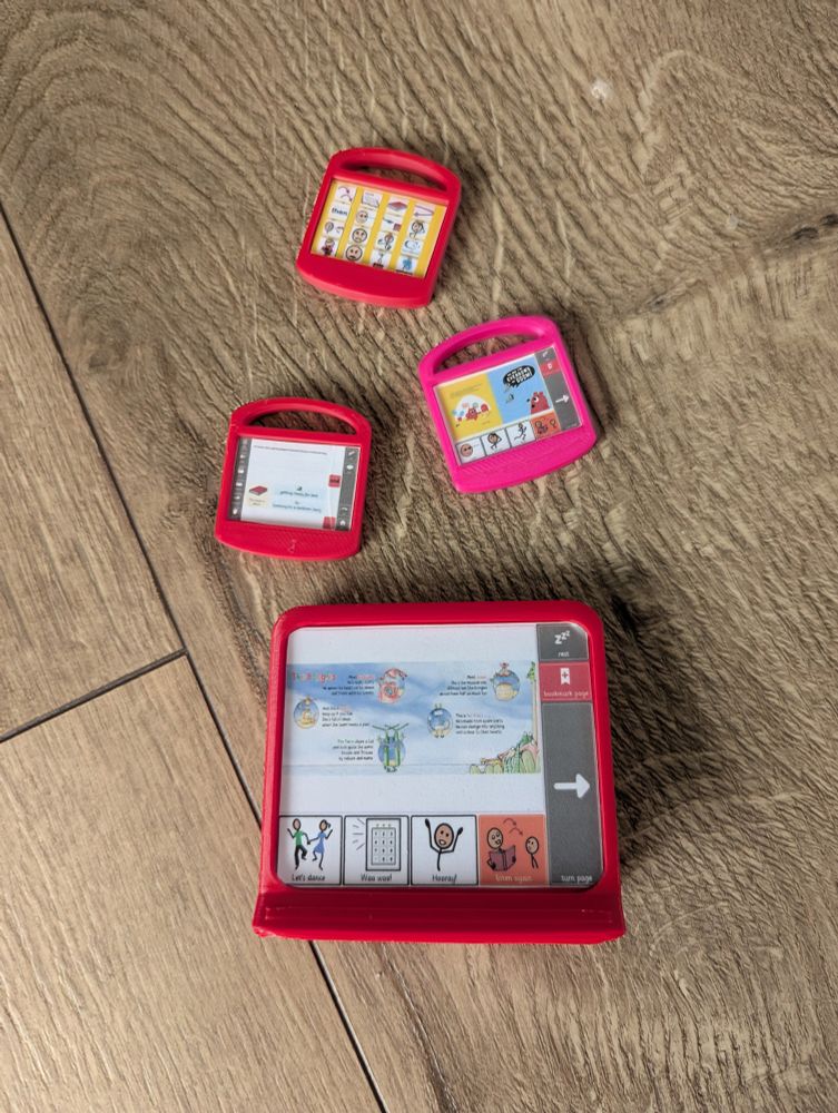 Photo of a 3D printed miniature toy eye gaze device and three 3D printed miniature toy iPads, all with printed screenshots of CALL Scotland Bookbug resources. 
