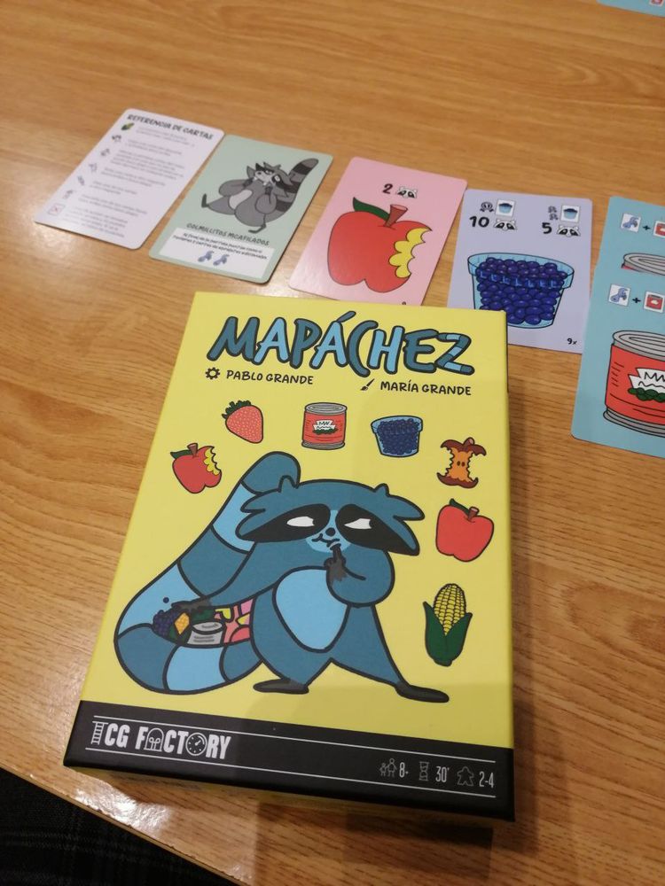 Portada del juego de cartas Mapachez. Tiene un mapache en la portada y manzanas, maíces, arándanos, latas de comida, fresas...