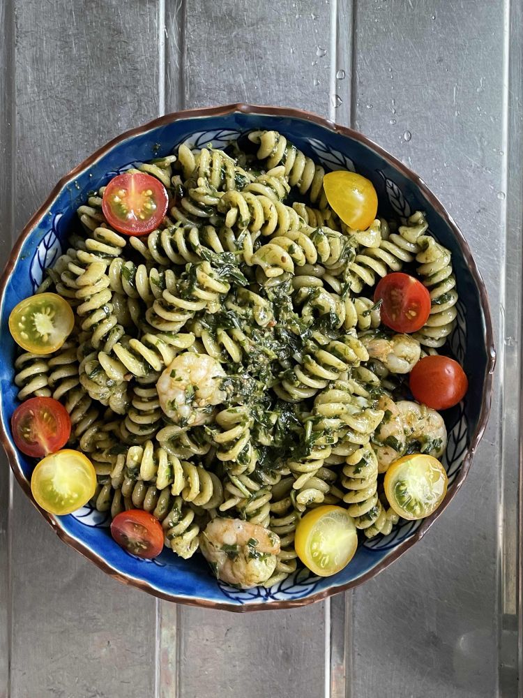 くるくるしたパスタ・フジッリとエビにジェノベーゼソースが絡んでいて、半分にカットされた赤と黄色のミニトマトがお皿の淵に沿って盛り付けられている。