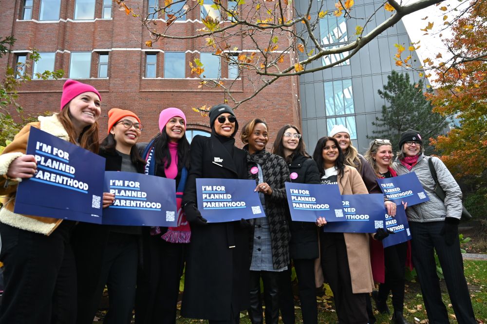 A photo of Attorney General Andrea Joy Campbell posing for a group photo with advocates and leaders of the sexual and reproductive health space, holding up blue signs that say "I'm for Planned Parenthood."
