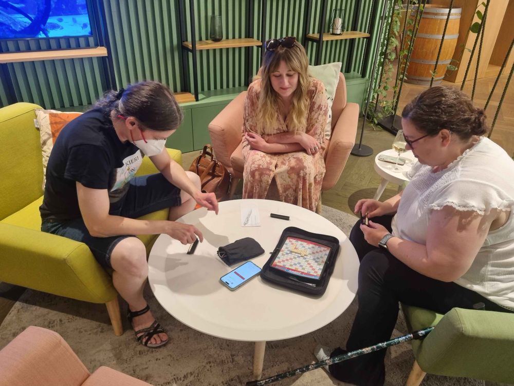 Real, Sulin and Mimkins looks very serious playing scrabble around a table in a lobby area. 