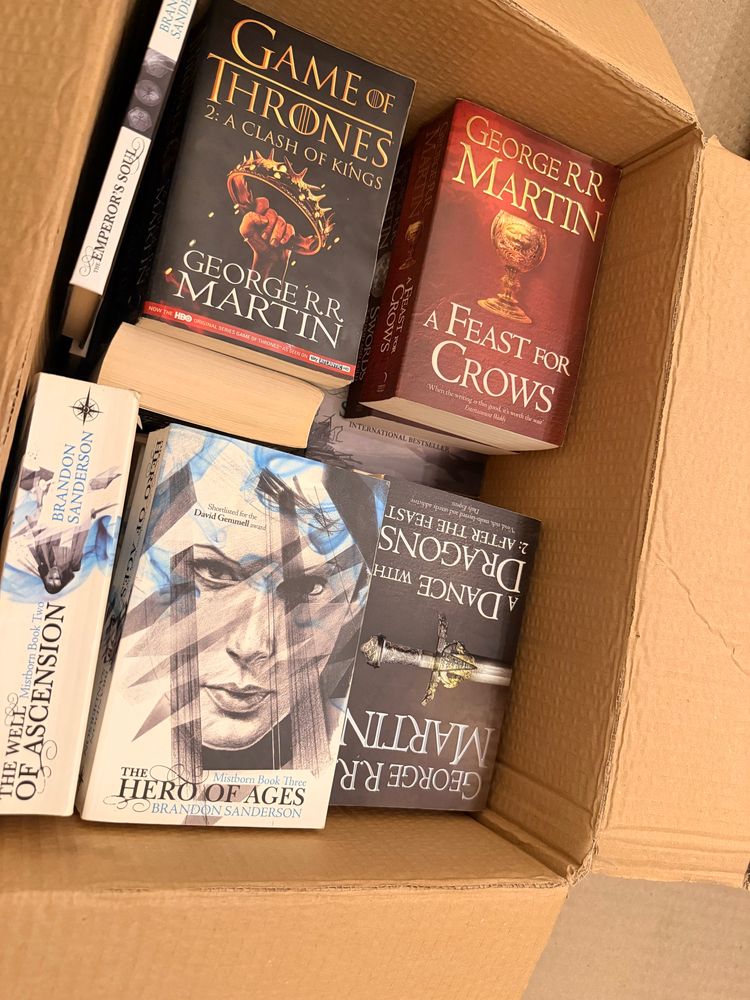 A cardboard box which is full of Brandon Sanderson Cosmere books and Game of Thrones books.