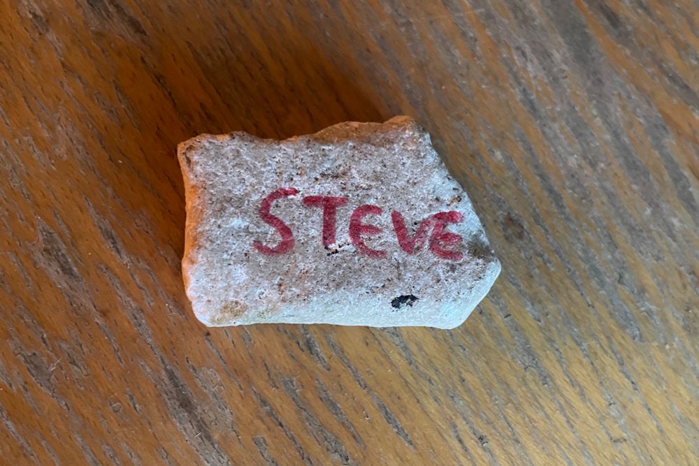 A jagged five sided flat rock with the word STEVE written on it in red felt tip
