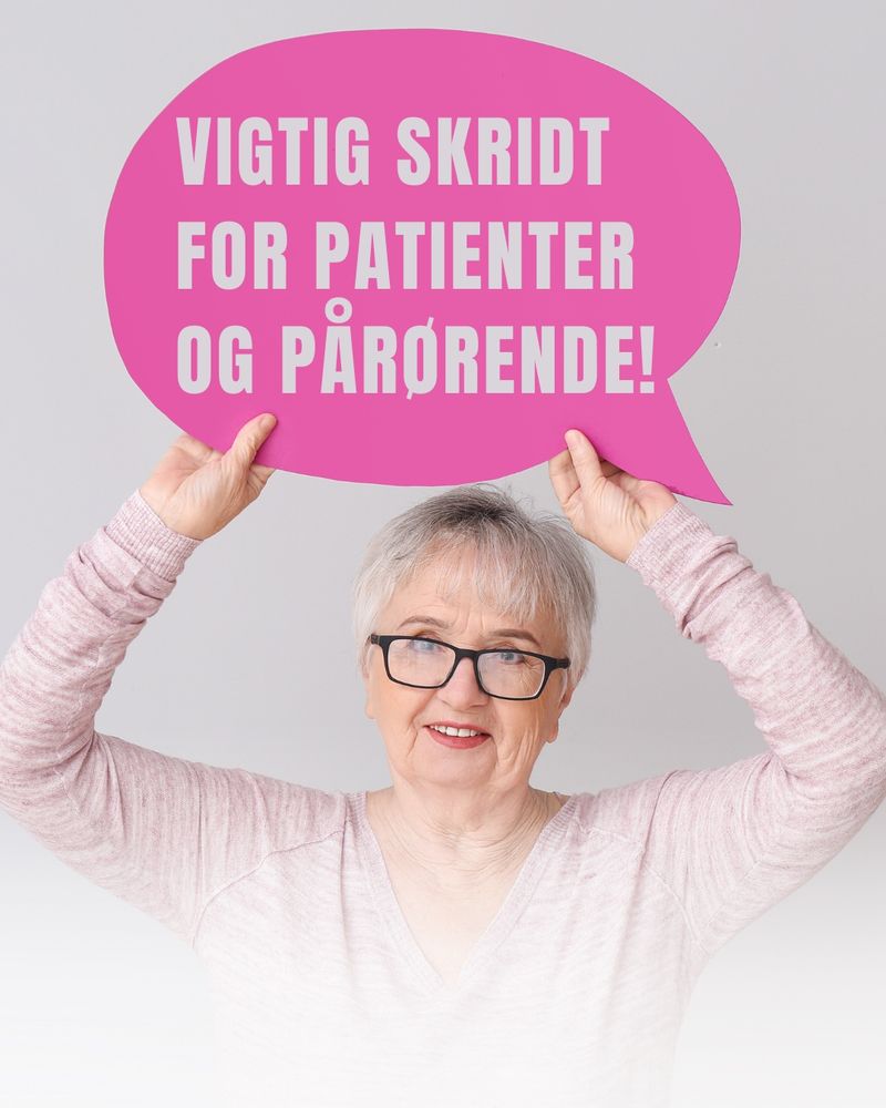 Billede af dame, der står med et skilt på det står der: Vigtigt skridt for patienter og pårørende 