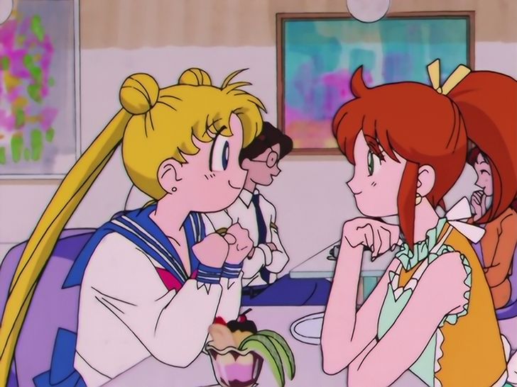 Usagi Tsukino em uniforma colegial conversa animada com Unazuki sentadas numa mesa da Frutaria Crown, onde Unazuki trabalha