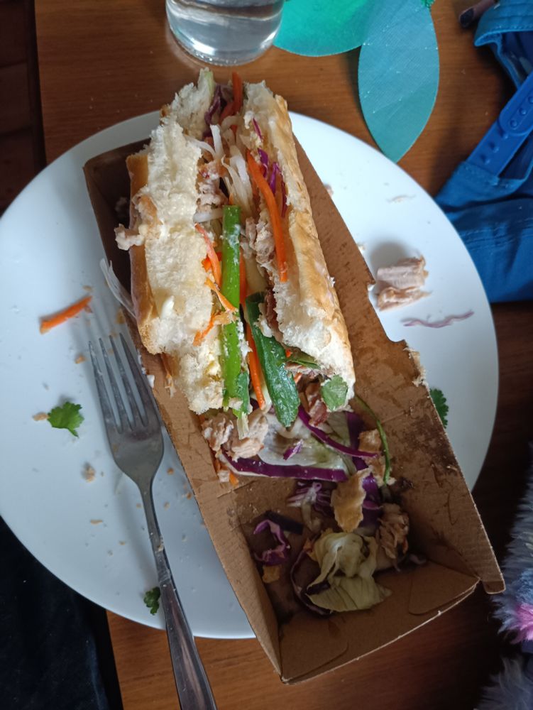 half a banh mi on a plate next to a fork , surrounded by debris
