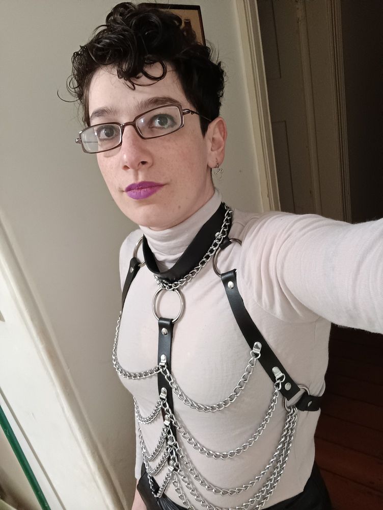 pale dark haired butch in a white skivvy and black leather harness with chains