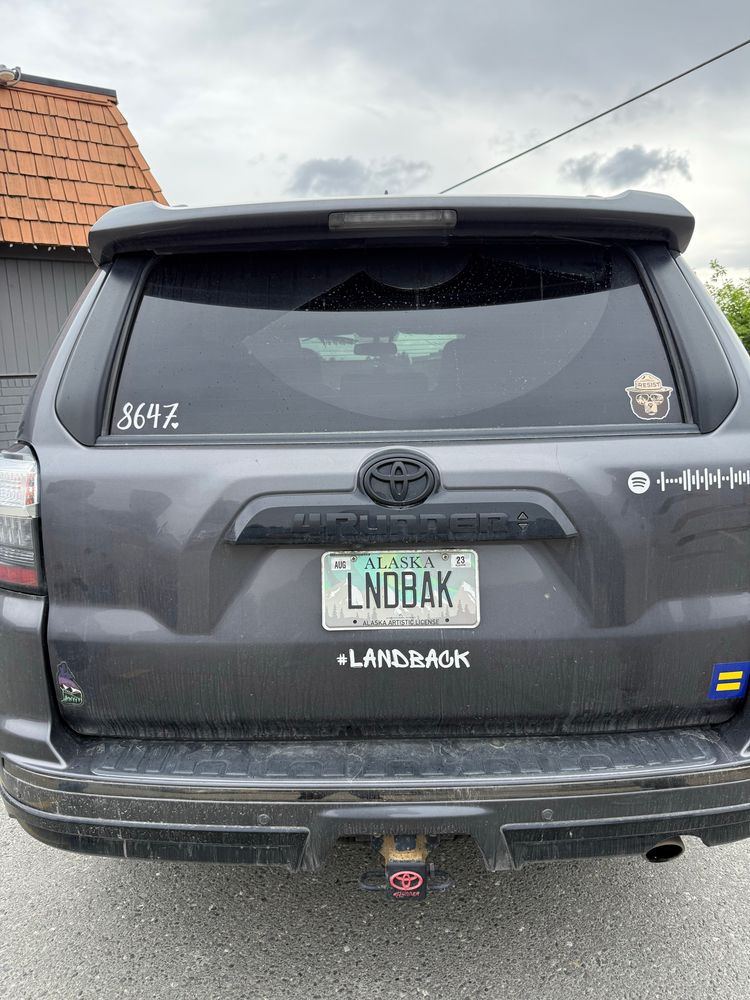 A black Ford 4-runner with several bumper stickers (including “8647”, the queer ally square one (not sure how to describe it, yellow with a blue border and blue line through the middle), smoky the bear, a Spotify (?) one that I don’t understand, and #landback. The license plate reads “LNDBAK”