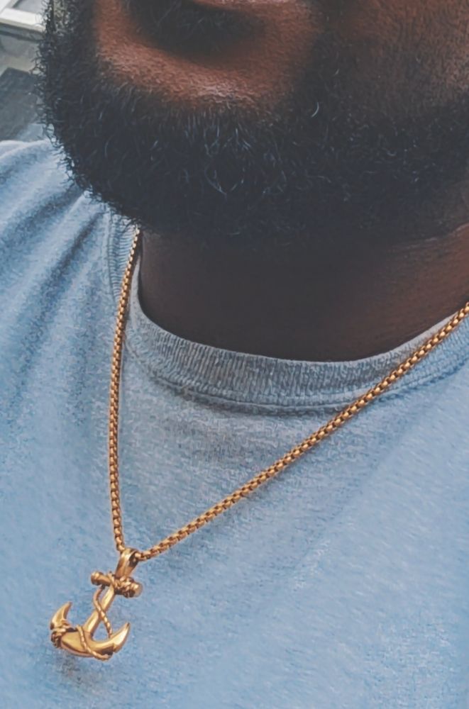 A closeup shot of the users lower jaw and upper bust, they're fashioning a short beard of black hair that's neatly trimmed. Adorning them is a light grey simple undershirt with a simple gold rope chain that carries an anchor pendant.