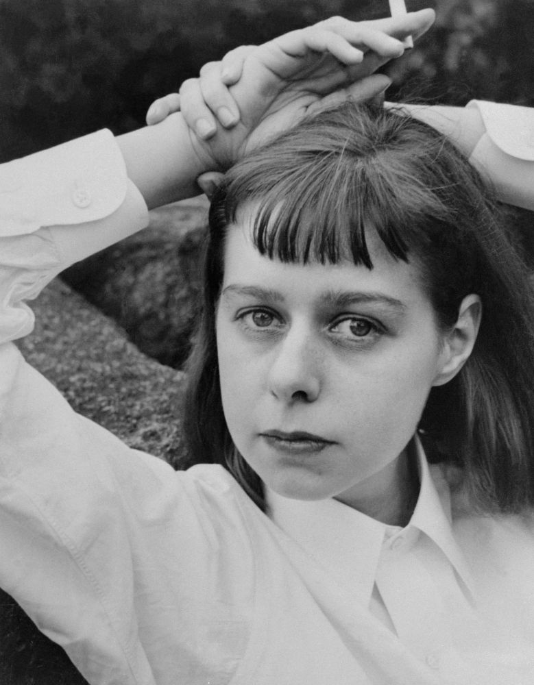 A young Carson McCullers, a white woman with a neat bob and bangs, wearing a crisp white shirt and holding a cigarette 