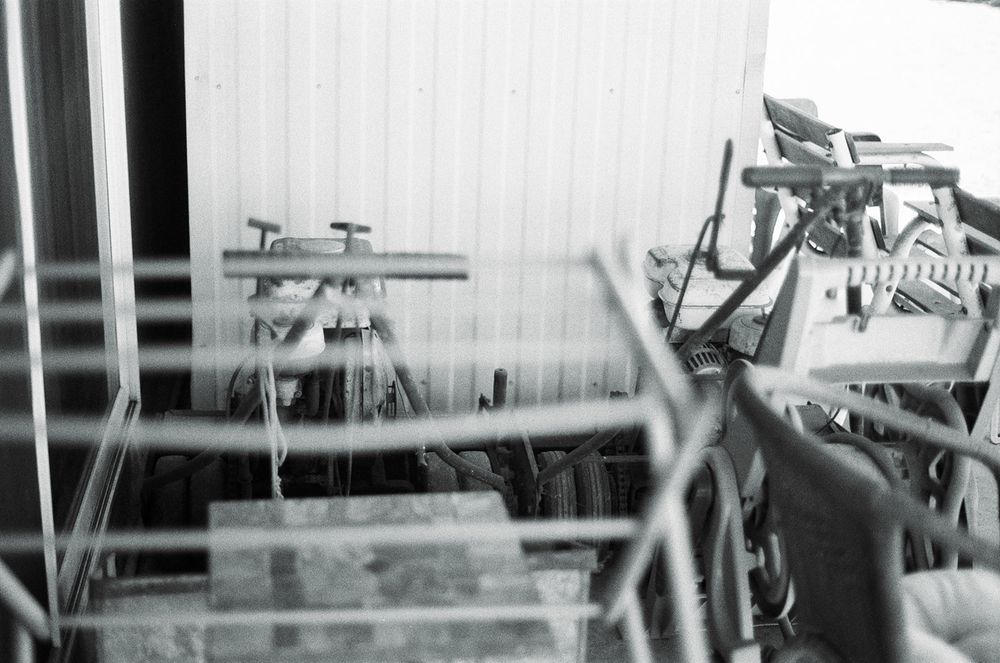 A bunch of rusty yard/gardening equipment and chairs next to a white metal shed 